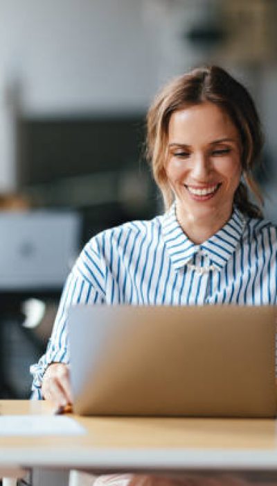 A smiling Caucasian entrepreneur reading something on his laptop while sitting at her office desk.